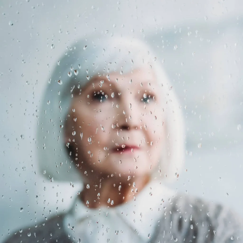 samotna seniorka za szybą z kroplami deszczu