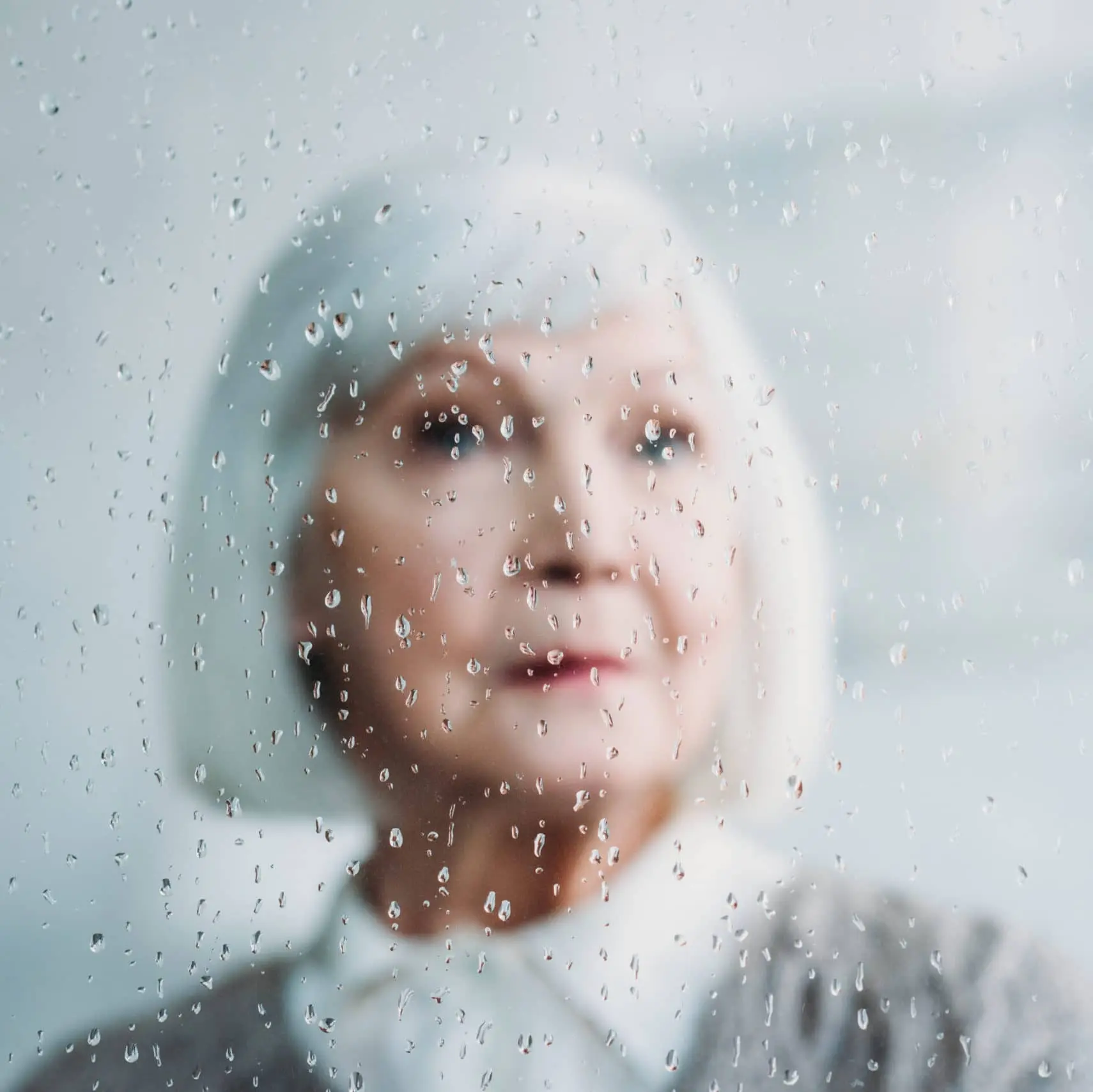 samotna seniorka za szybą z kroplami deszczu