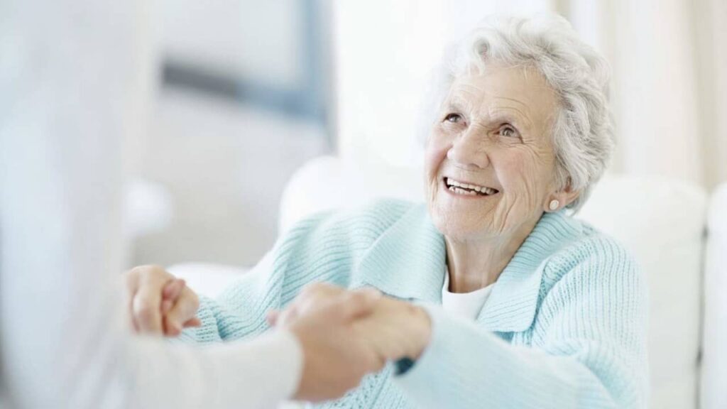 uśmiechnięta seniorka trzyma za ręce opiekunkę